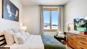 Una camera da letto con un letto, una cassettiera, una sedia, una scrivania, una lampada, un quadro e una finestra con vista.
