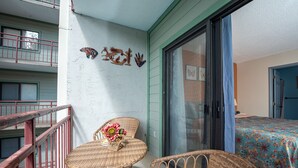 A balcony with wicker furniture, a glass door leading to a bedroom, and a wall with decorative elements.