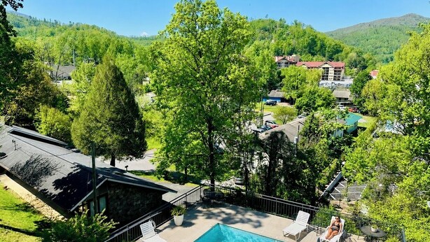 A swimming pool with lounge chairs, surrounded by greenery and a view of a hillside.