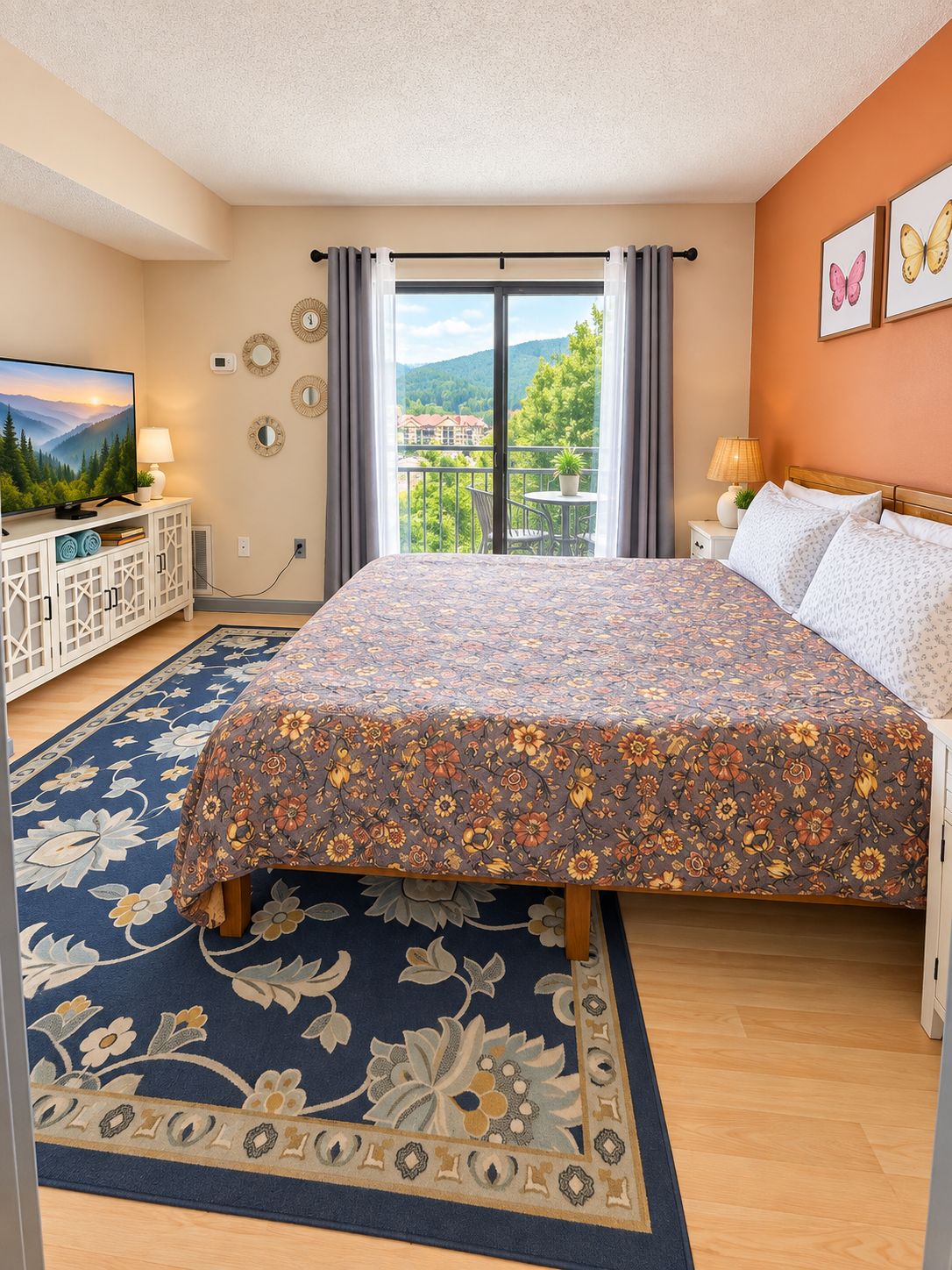 Ein Schlafzimmer mit Bett, Fernseher, einem Balkon mit Blick und einem gemusterten Teppich.