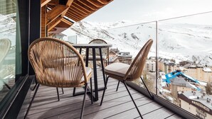 Un balcon doté d’un plancher en bois, de deux fauteuils en osier et d’une table.