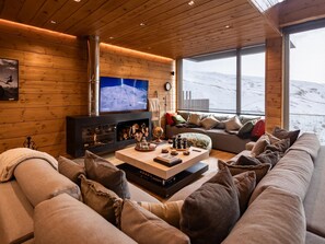 A cozy living room with a fireplace, a large TV, and a sofa with cushions. - Arttysur Lux - Best 4 BDRM Villa in Sierra Nevada (Sierra Nevada)