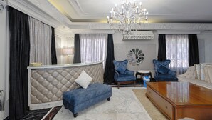 Een weelderige woonkamer met een gestofte bank, een blauwe fauteuil, een houten salontafel en een kroonluchter.