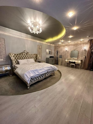 A luxurious bedroom with a large bed, a vanity with a mirror, and a chandelier.