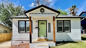 Una casa de un piso con puerta verde, un letrero de bienvenida y un pequeño porche con escalones.