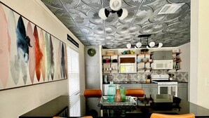 Una cocina moderna con microondas, estufa y varios utensilios de cocina en estantes. Hay una zona de comedor con dos sillas naranjas y una mesa.