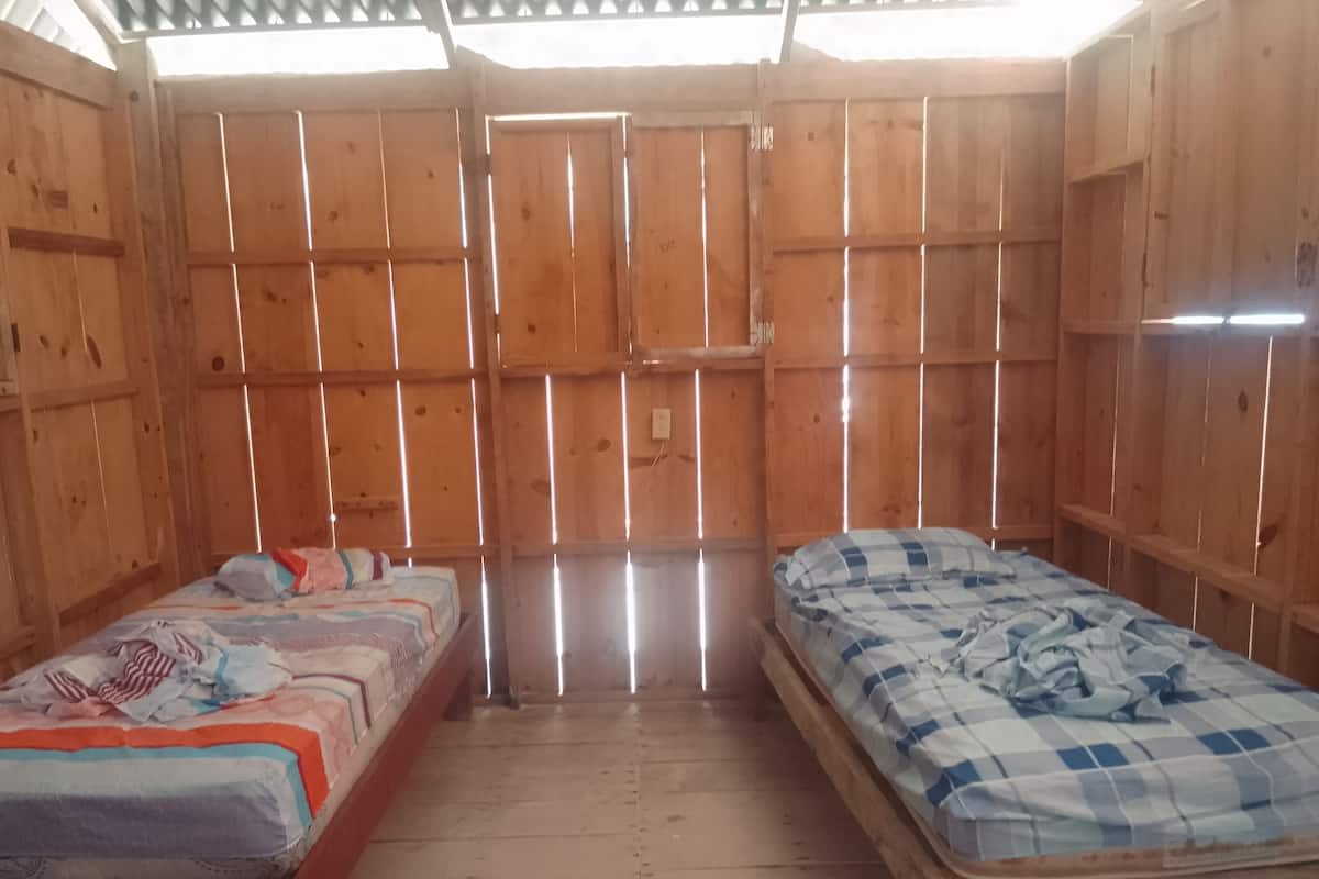 Um quarto pequeno de madeira com duas camas, piso de madeira e teto inclinado.