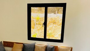 Een woonkamer met een zithoek, een bankje en een raam met uitzicht op een tuin.