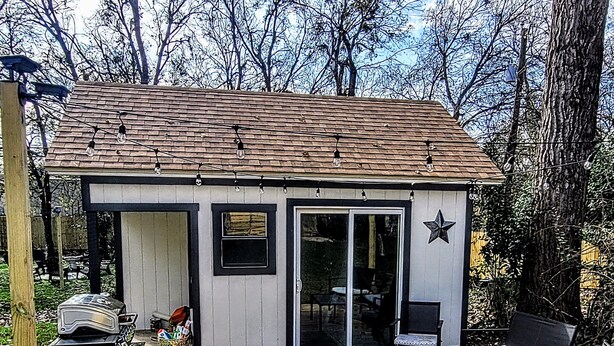 A small, single-story building with a sloped roof, a sliding glass door, and a star decoration on the wall. There is a deck with outdoor furniture and a grill cart. - Texas Sunshine Oasis WACO/Silos/Baylor: Pool, Piano, PingPong, Pets on 1/2 acre (Hewitt)