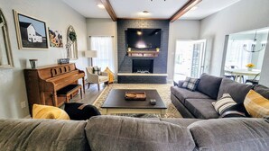 A living room with a fireplace, a ceiling fan, and a dining area with a table and chairs. - Texas Sunshine Oasis WACO/Silos/Baylor: Pool, Piano, PingPong, Pets on 1/2 acre (Hewitt)