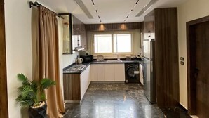 A modern kitchen with dark marble flooring, a central island, and a built-in oven. - Villa in palm hills-the crown (6th of October City)