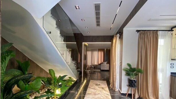 A modern interior with a marble floor, a staircase, and a living area with a sofa and curtains. - Villa in palm hills-the crown (6th of October City)