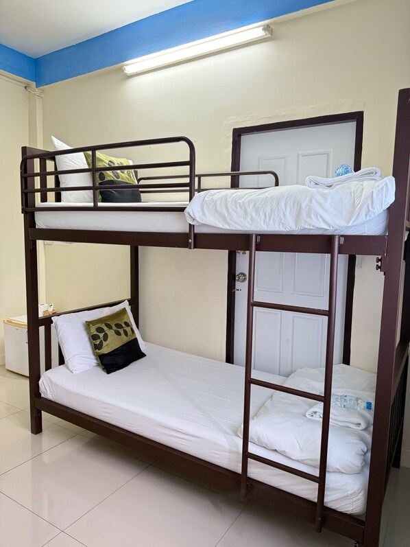 A bunk bed with white bedding and a ladder, a white door, and a blue ceiling light.