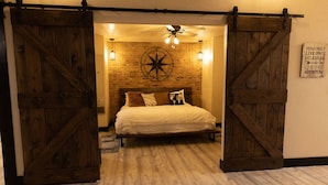 A bedroom with a bed, wooden doors, a brick wall, a compass decoration, and a motivational sign.