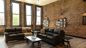 A spacious living room with leather sofas, a coffee table, and a brick wall adorned with framed pictures.