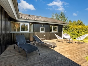A wooden deck with lounge chairs and a small table, a building with large windows, and a clear sky. - "Anca" - 450m from the sea by Interhome (Glesborg)