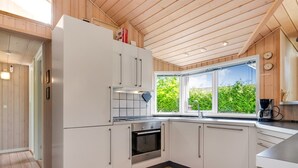 A modern kitchen with wooden flooring, white cabinetry, a built-in oven, and a window with a view of greenery.