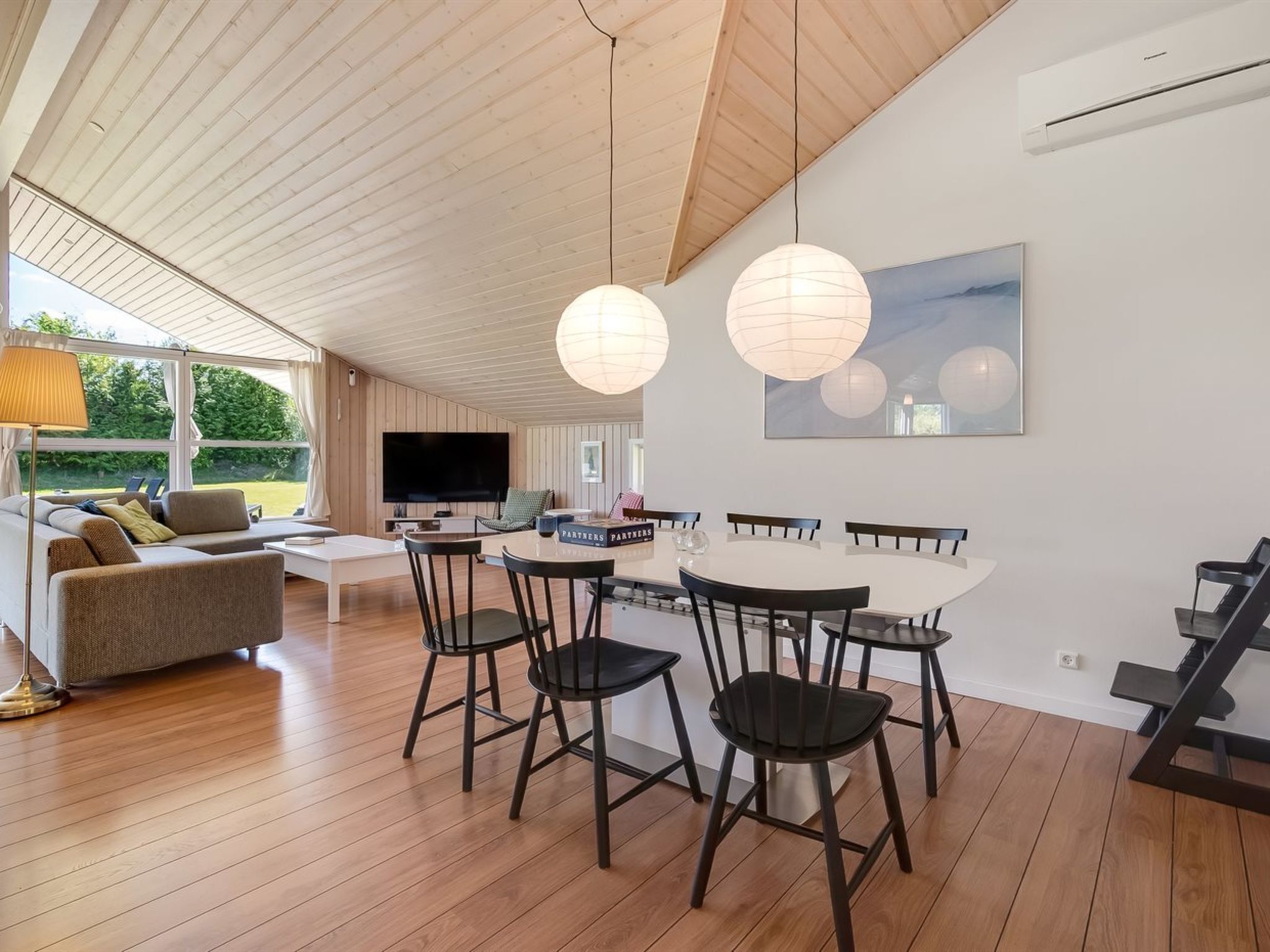 A modern living room with a sofa, TV, dining table with chairs, and a large window.