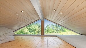 A room with a sloped ceiling, wooden flooring, and large windows offering a view of trees.