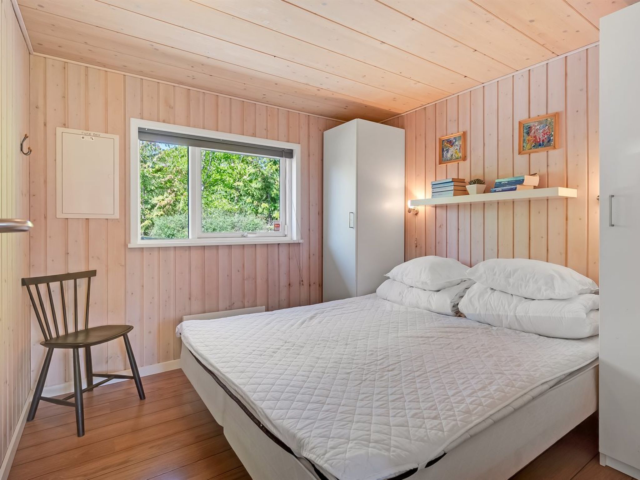 A bedroom with a bed, a chair, a window, and a shelf with books.