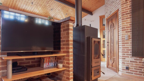 A modern living room with a flat-screen TV, a fireplace, and a brick wall. - Authentic House With Playroom and Infrared Sauna (Bilzen)