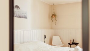 A bedroom with a bed, a chair, a bedside table with a candle, and a hanging plant. - Authentic House With Playroom and Infrared Sauna (Bilzen)