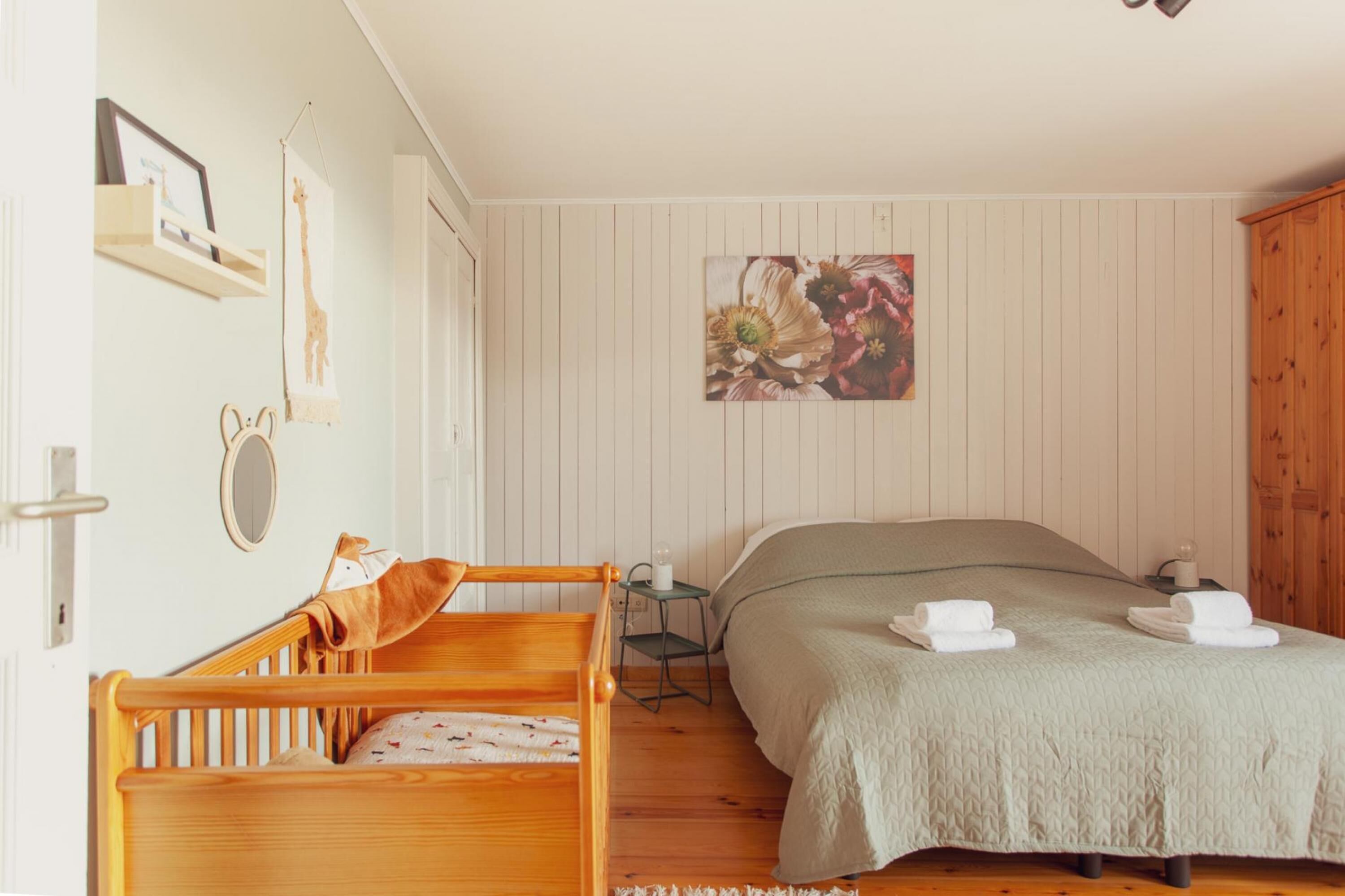 A bedroom with a wooden bed, a small bedside table, a wall-mounted shelf, and a framed picture.