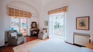 A bedroom with a large bed, two chairs, a table, and a window with a view. - Villa White by Elite Villas (Capri)