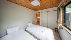 Un dormitorio con dos camas, techo de madera, una ventana con cortinas y una puerta que da a otra habitación.