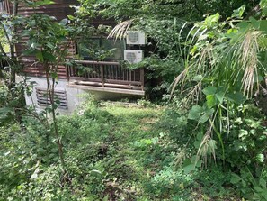 A lush garden with dense foliage, a wooden deck, and an air conditioning unit. - Wakuraba (Hakuba)