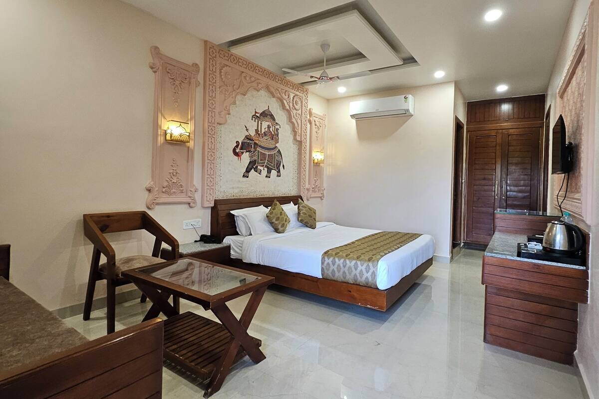 Une chambre d’hôtel comprenant un lit, un bureau en bois, une chaise, un petit coin cuisine et des œuvres d’art décoratives sur les murs.