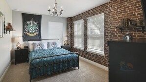 Ein Schlafzimmer mit Metallbettgestell, einer Kristallleuchtre, Wandteppich und Backsteinwand.