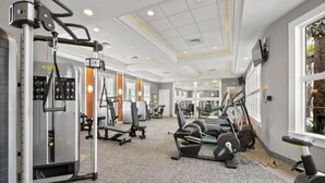 Ein Fitnessstudio mit verschiedenen Trainingsgeräten, einem großen Fenster mit Blick und einer Decke mit Einbuchtungslichtern.