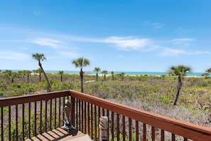A wooden deck with a view of a beach and palm trees.