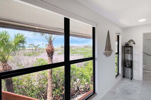 A hallway with large windows, a marble floor, and a view of a landscaped area with trees.