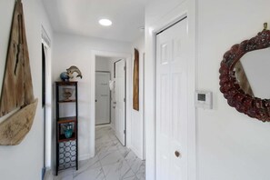 Ein Flur mit weißen Wänden, einem Holzregal mit Dekoration, einem großen Spiegel und einem Thermostat.