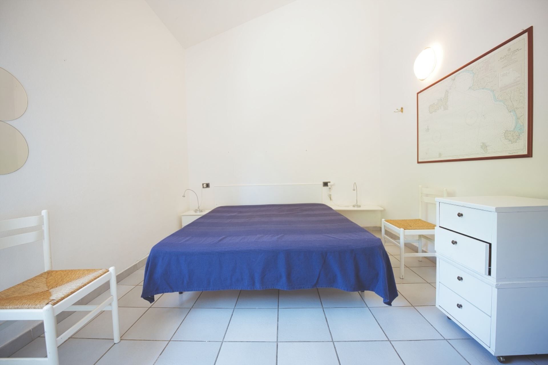 Une chambre à coucher avec un lit, une commode blanche, une chaise et une carte accrochée au mur.