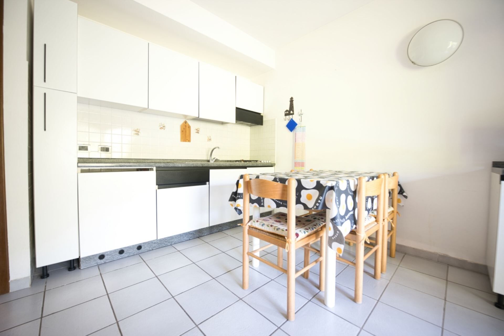 Een kleine keuken met witte kasten, een betegelde vloer en een tafel met een bloemenlaken.
