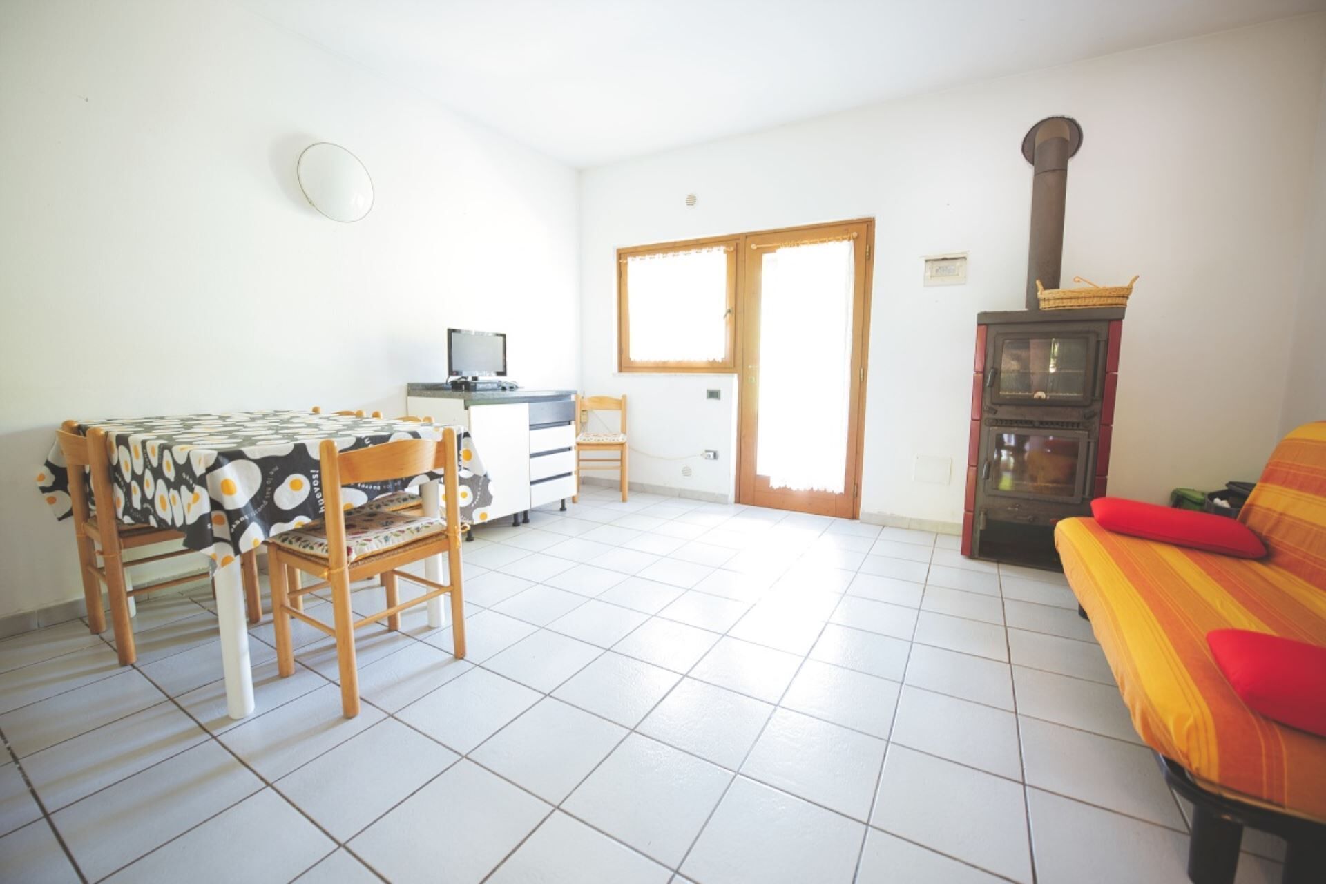 A room with a dining table, chairs, a sofa, a television, a fireplace, and a door with windows.