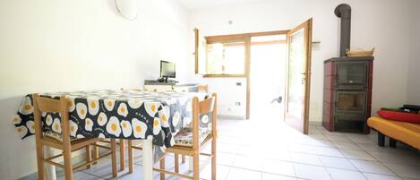 A dining area with a table and chairs, a television, and a wood-burning stove.