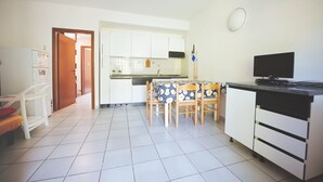 A compact kitchen with white cabinets, a tiled floor, a dining table with chairs, a television, and a refrigerator. - Casa Pamalù 5 with pool in the beautiful bay of Nisporto (Rio dell'Elba)