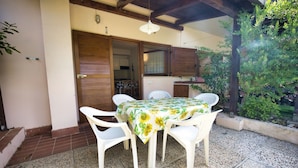 A patio with a table and four chairs, a wooden door, and a small kitchen area visible through an open door. - Casa Pamalù 5 with pool in the beautiful bay of Nisporto (Rio dell'Elba)