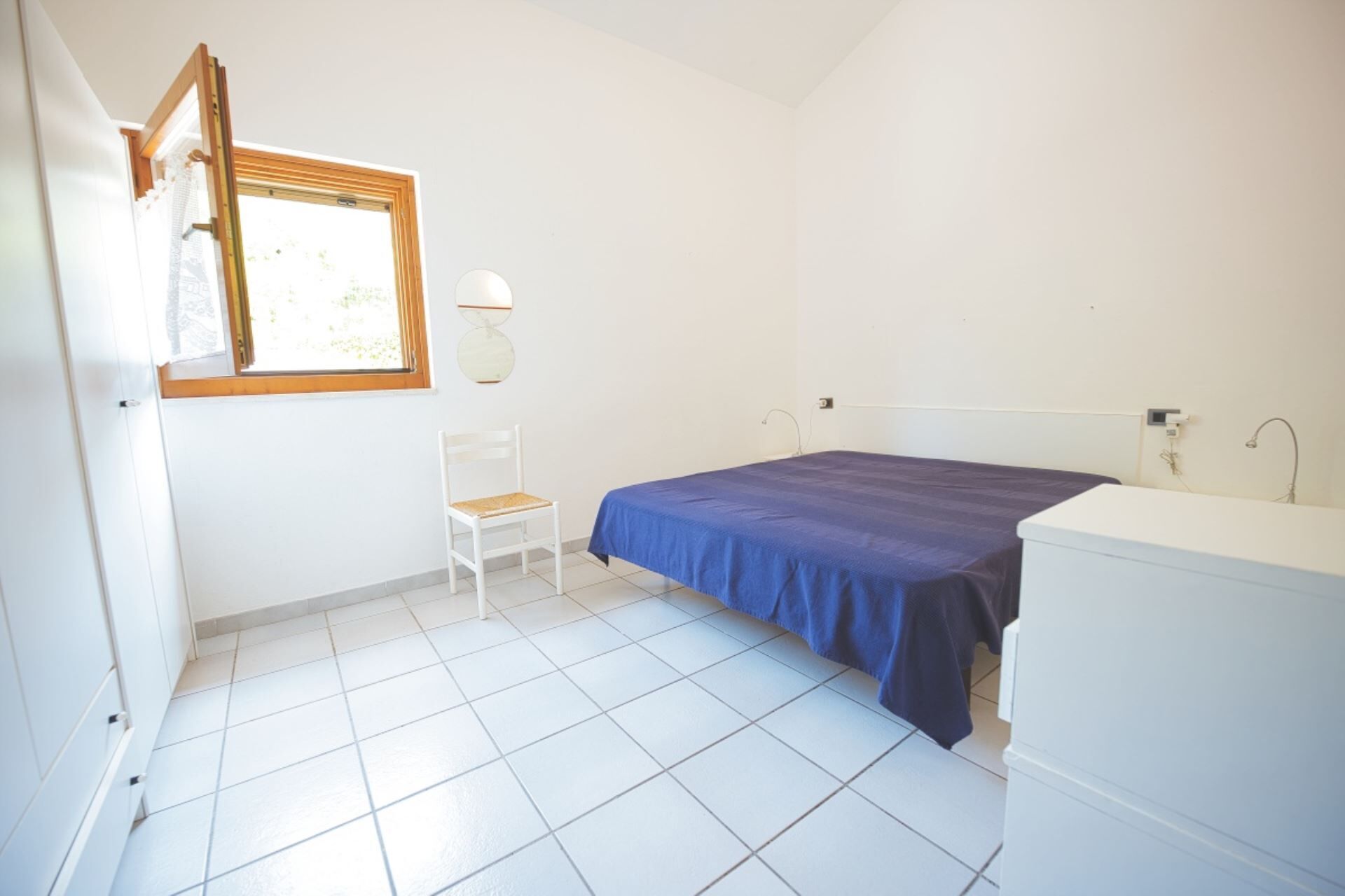 Una habitación pequeña y limpia con cama, una silla, una ventana y un espejo.