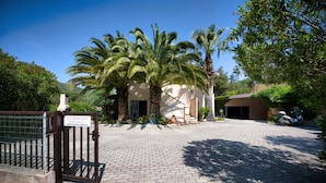 A gated entrance to a property with a paved driveway, palm trees, and a sign indicating a residence named "Palmu". - Casa Pamalù 5 with pool in the beautiful bay of Nisporto (Rio dell'Elba)