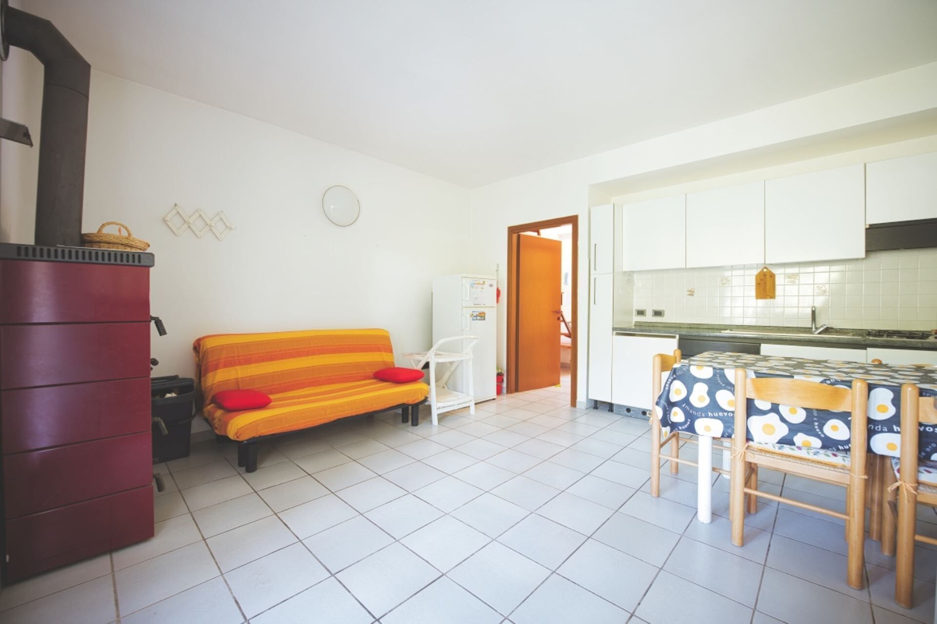 Een compacte woonruimte met een bank, een eettafel met stoelen, een keukenhoek en een rode kast.