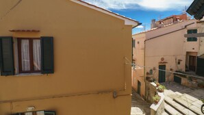 Eine schmale Straße mit Gebäuden an beiden Seiten, mit einem kleinen Fenster mit Fensterläden und einer sichtbaren Tür.
