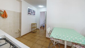 Eine kleine Küche mit Gaskochfeld, einem Esstisch mit grüner Tischdecke und einem kleinen Holzschemel.