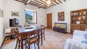 A spacious living room with a wooden dining table, chairs, a sofa, and a bookshelf. A television is on a stand, and a window offers a view of the outside. - Casa al secco apartment with sea view in the heart of Rio Marina (Rio Marina)