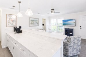A modern kitchen with a large island, pendant lights, a ceiling fan, and artwork on the walls.