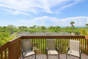A deck with three chairs facing a beach view.